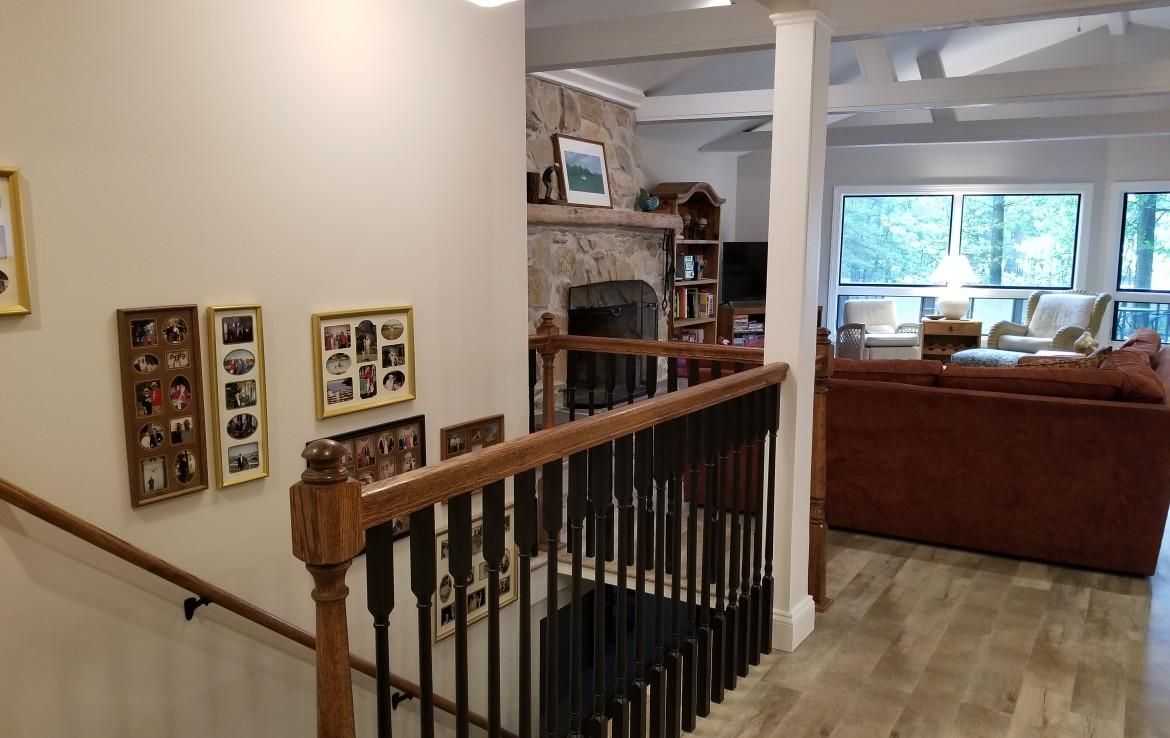 Interior view of a hallway and stairs leading to a living room with a fireplace, brown couch, and large windows.