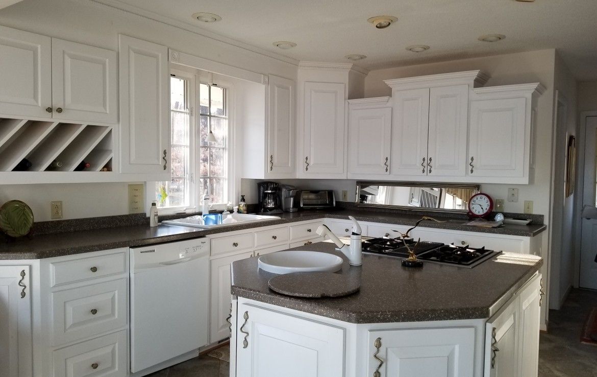 White kitchen with granite countertops, island with stovetop, cabinets, and a window.