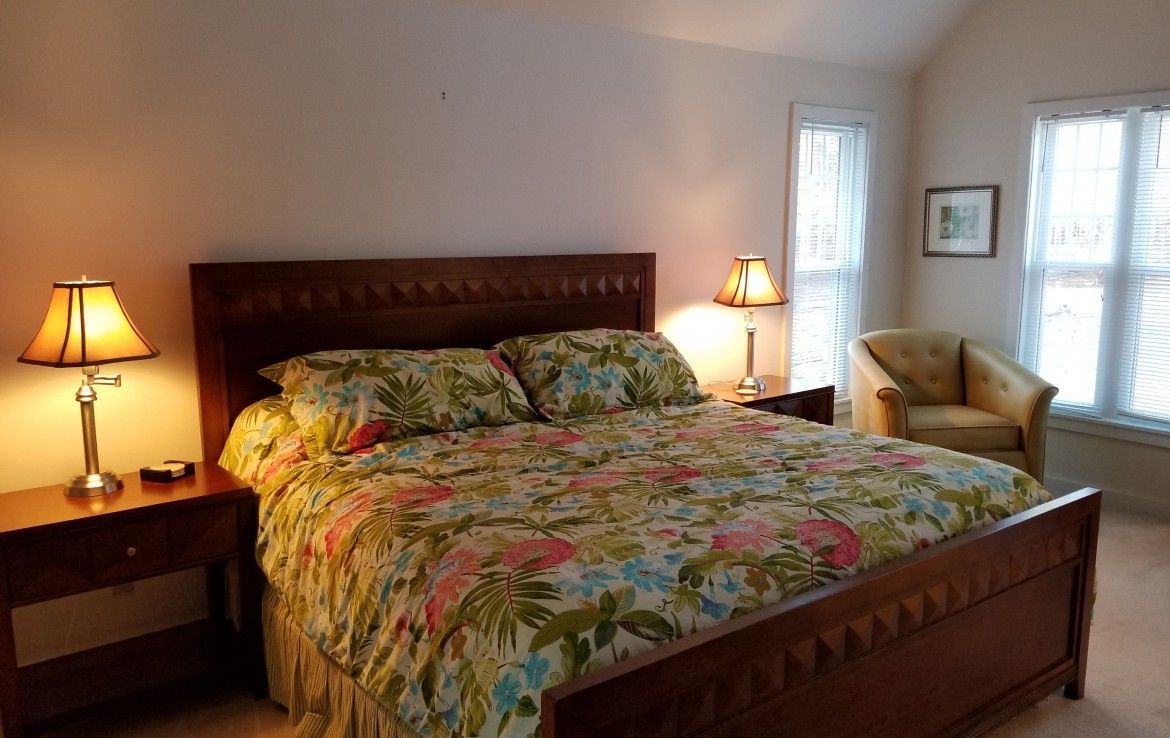 Bedroom with wooden bed and nightstands, floral bedding, lamps, and a chair.