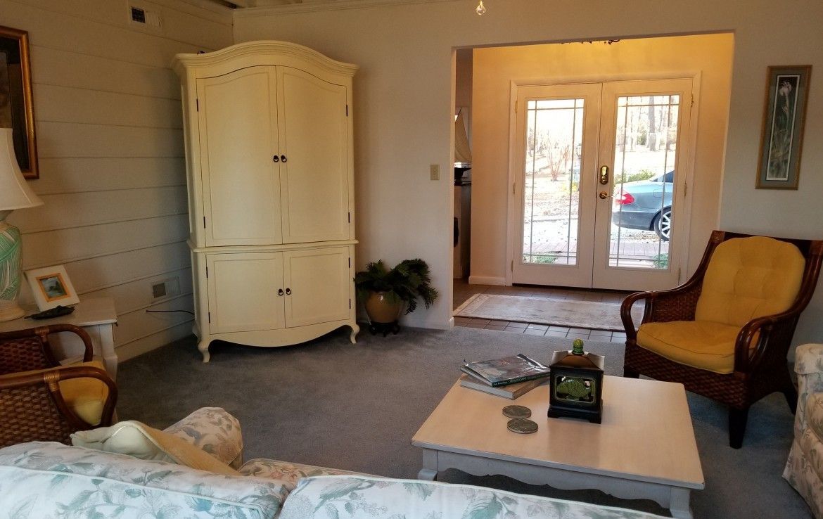 Living room with ivory armoire, wicker chair with yellow cushion, and French doors.
