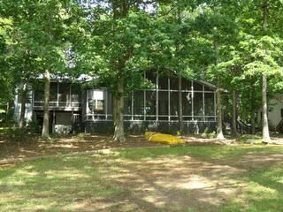 Cabin in a wooded area with a screened porch and green grass in front.