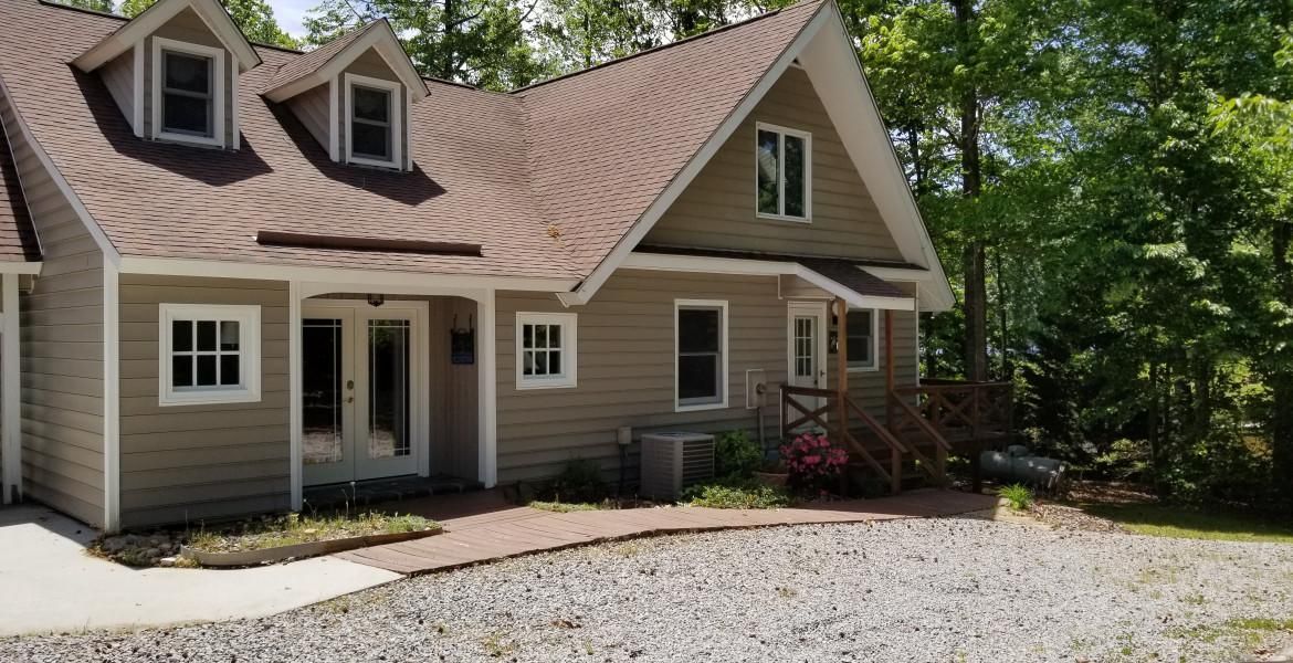 Tan-colored house with brown roof and multiple windows, surrounded by trees.