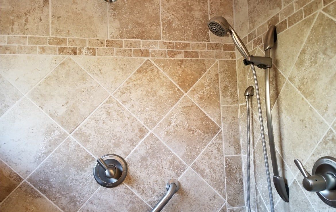 Tiled shower with handheld showerhead, wall-mounted controls, and grab bar.