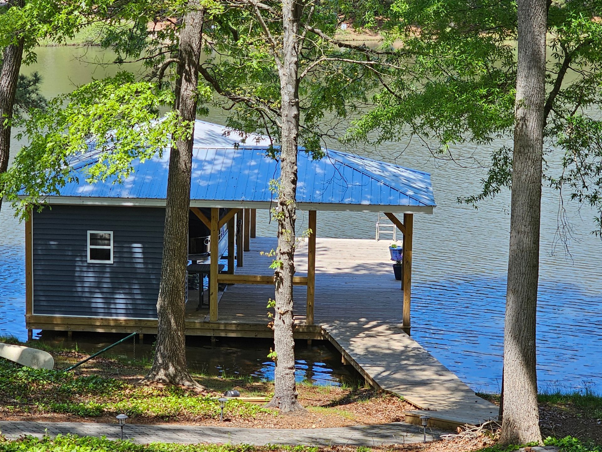 Dock with blue roof over calm water, surrounded by trees.