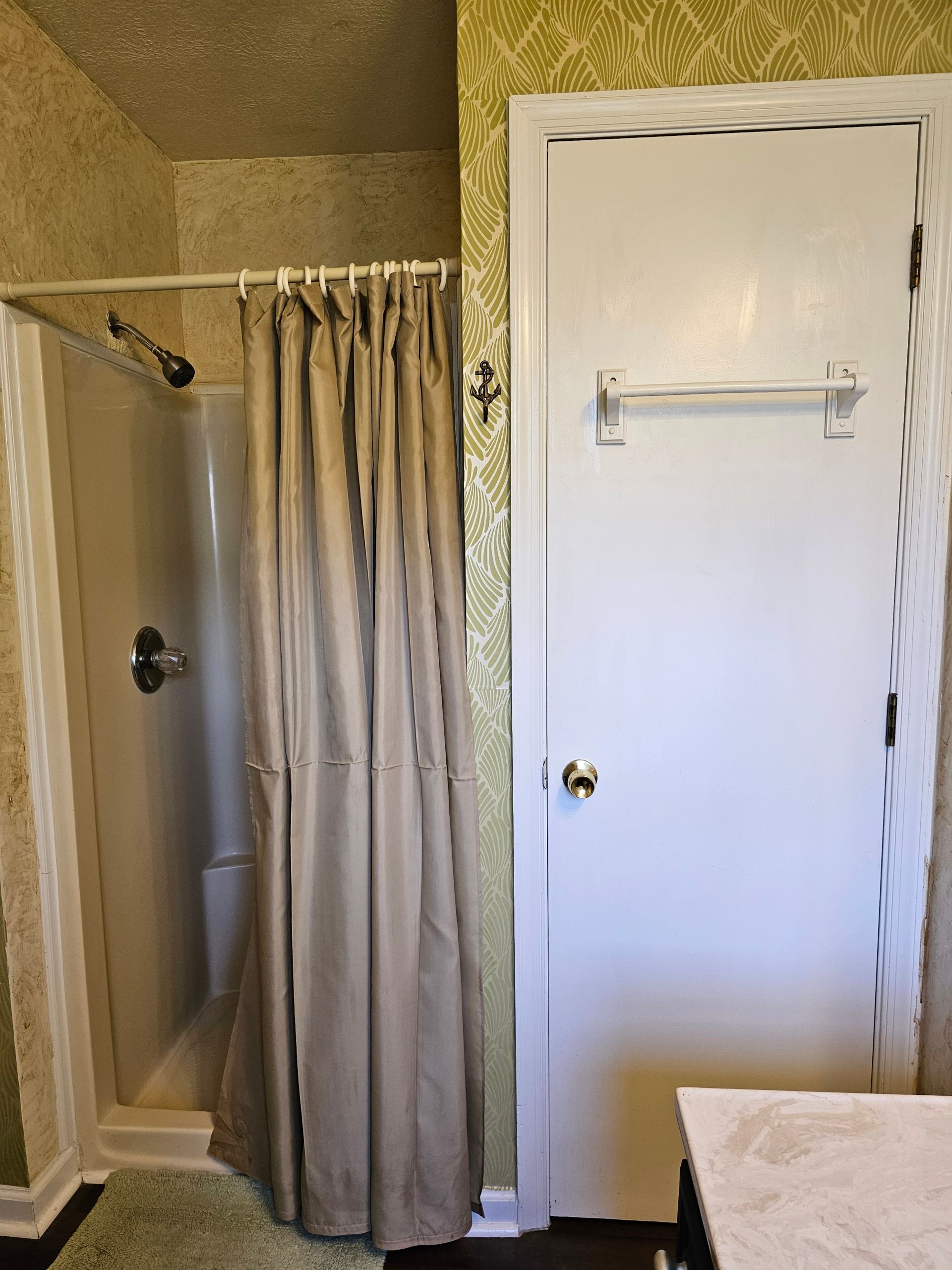 Bathroom with shower, white door, and floral wallpaper. Light brown shower curtain.