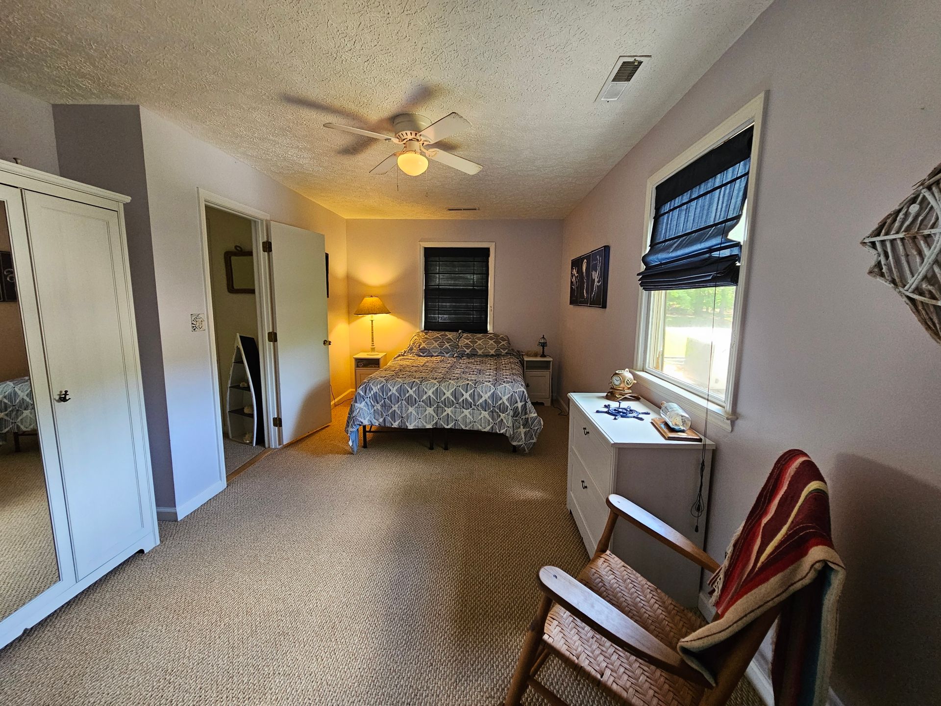 Bedroom with bed, closet, and chair. Walls are light purple; a window with shades is visible.