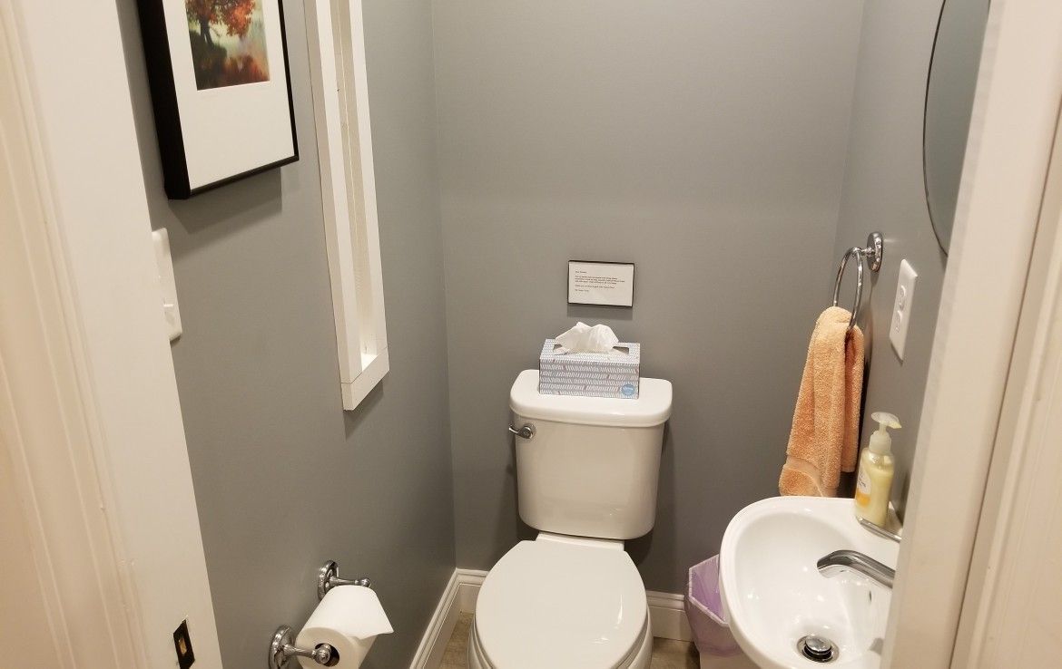 Small bathroom with gray walls, toilet, sink, and artwork.