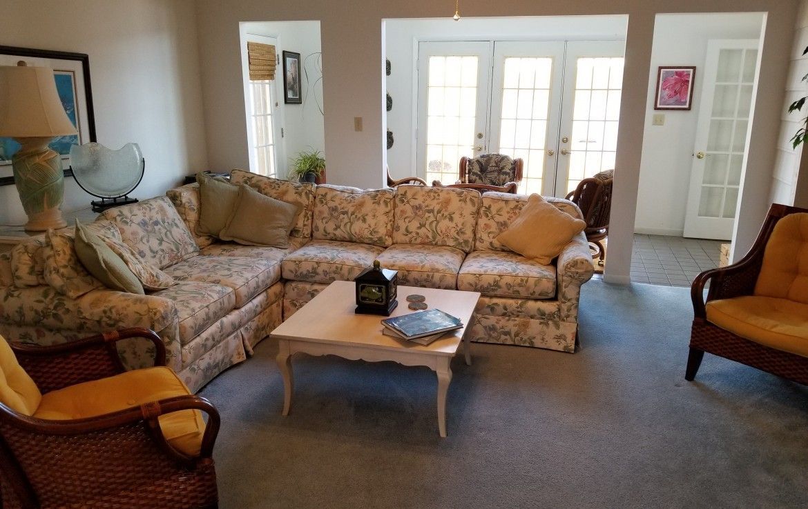 Living room with floral couch, coffee table, and wicker chairs; French doors visible.