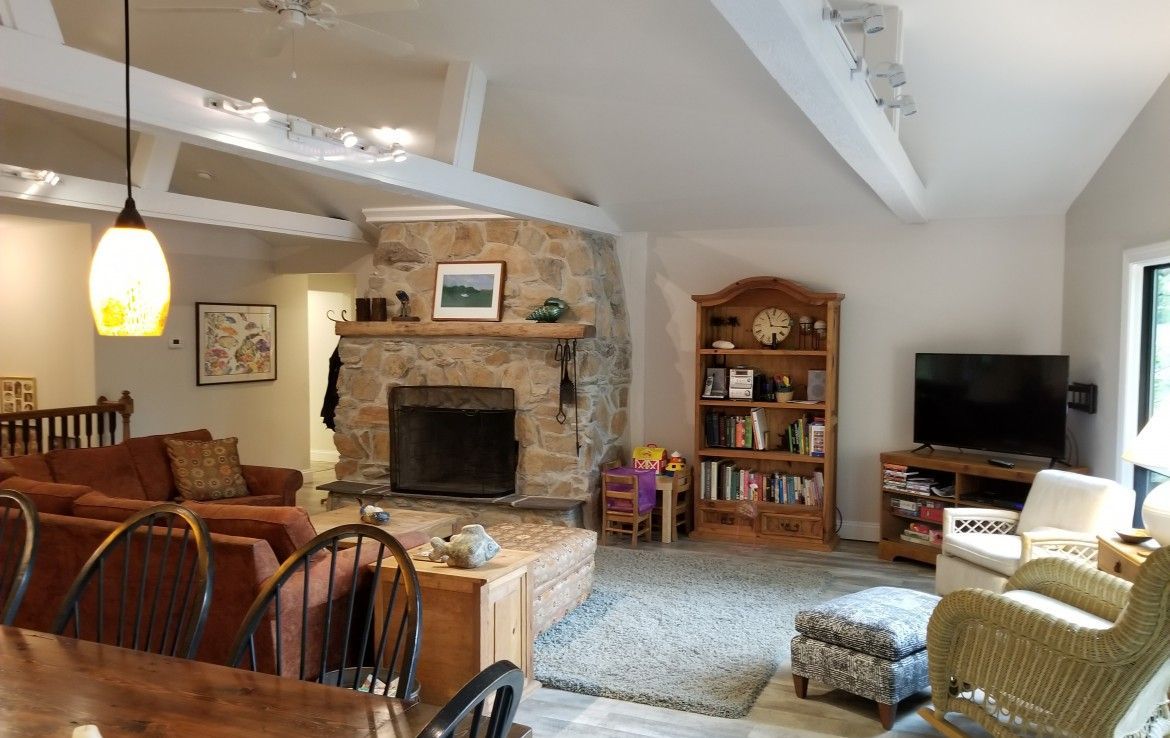 Cozy living room with stone fireplace, wood beams, and open floor plan, with sofa, bookshelves, and TV.