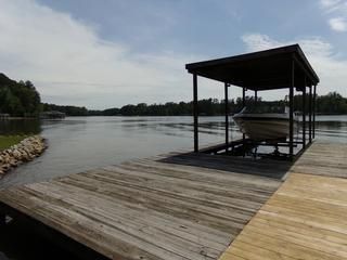 Wooden dock with boat lift holding a boat, overlooking a lake under a cloudy sky.