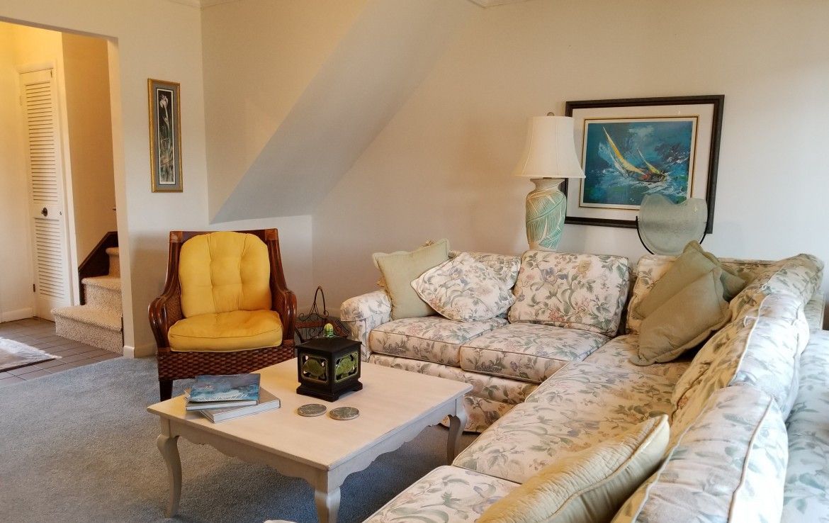 Cozy living room with floral sectional sofa, yellow armchair, and white coffee table under a sloped ceiling.