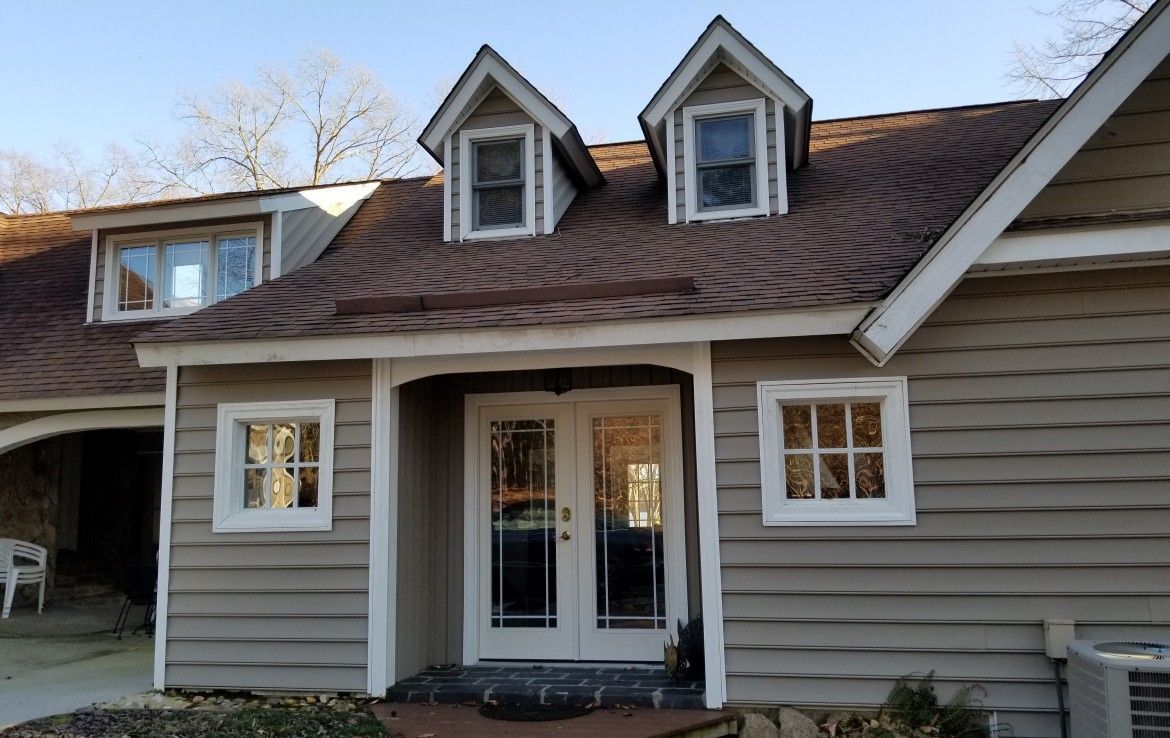 Tan house with a brown roof and dormer windows. Two front doors, and light siding.