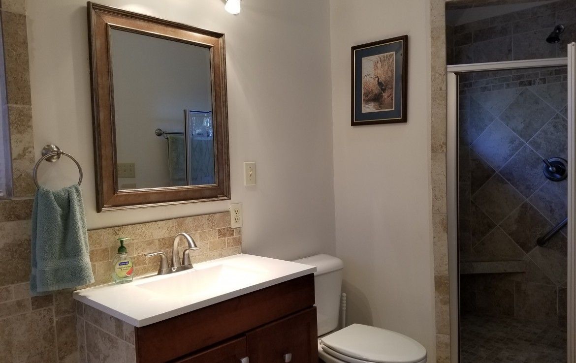 Bathroom with a dark wood vanity, white countertop, square mirror, and a tiled shower.