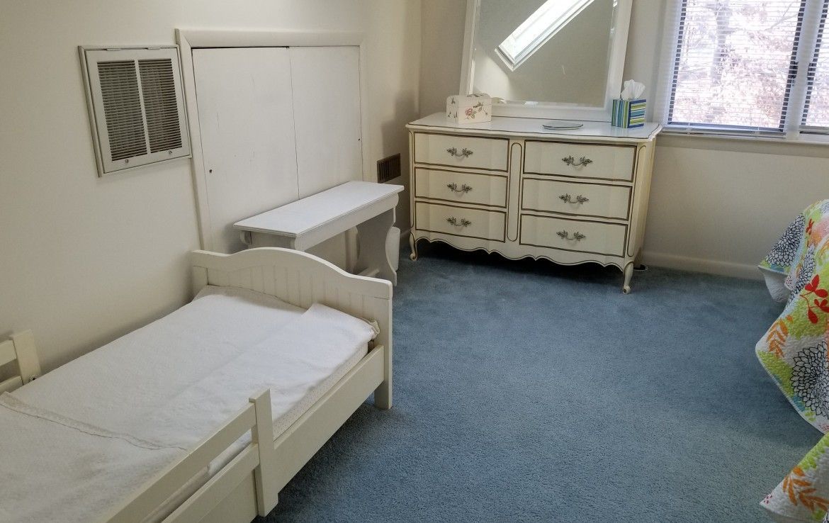 Bedroom with twin bed, dresser, desk, and window. Blue carpet, white furniture, and a mirror.