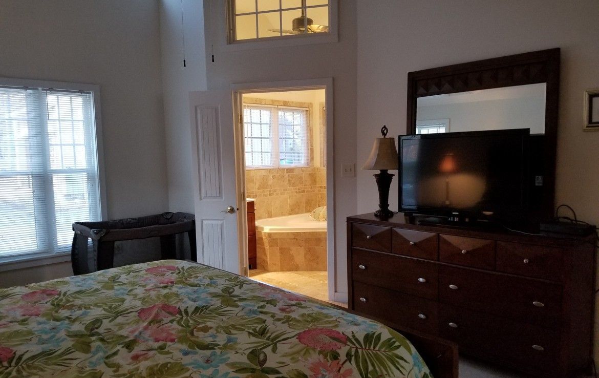 Bedroom with bed, dresser, TV, and en-suite bathroom visible through doorway.