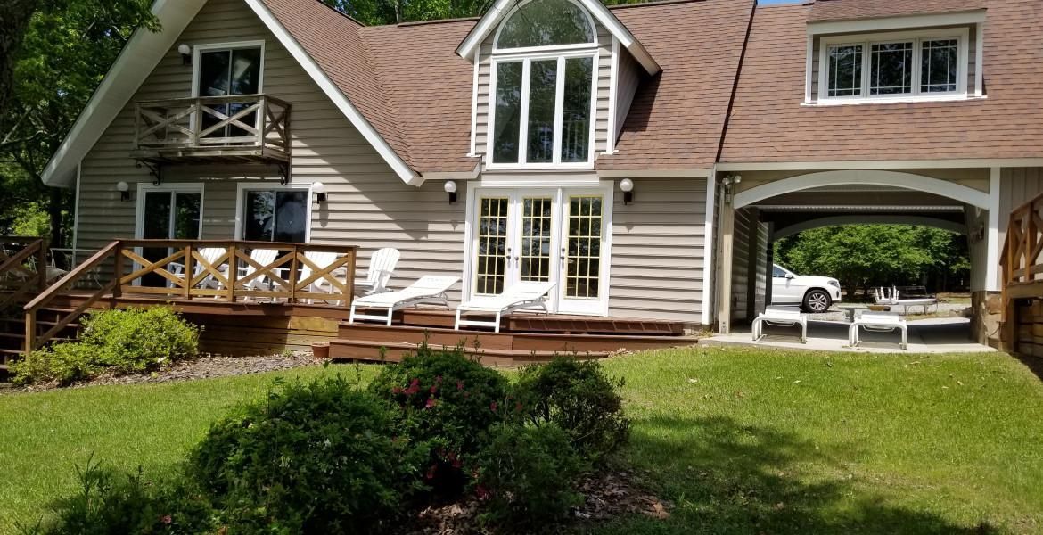 Tan house with brown roof, open air garage, and wooden decks.