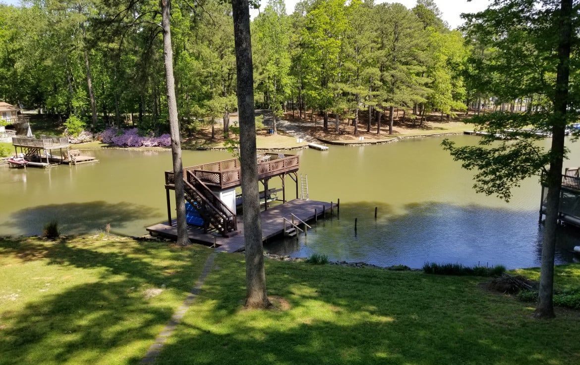 Lakeside dock with covered deck. Overcast water, green grass, and trees. Sunny day.