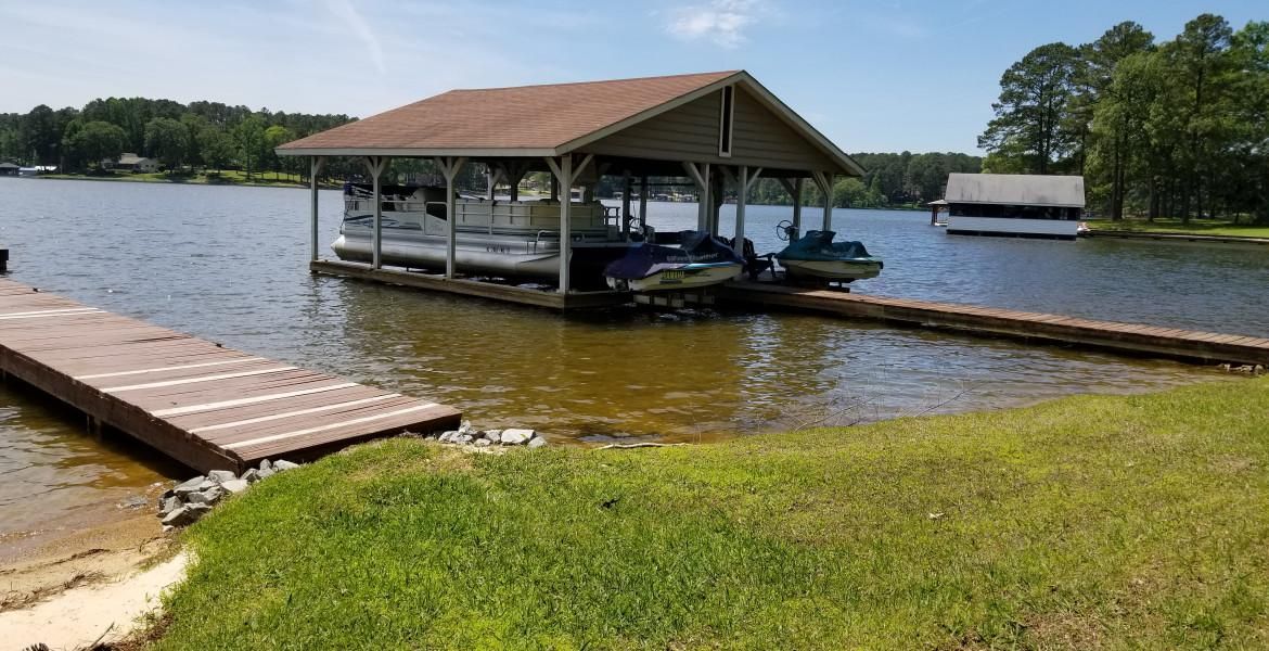 A boat dock with boats on a lake, with a covered boat slip and a dock extending into the water.