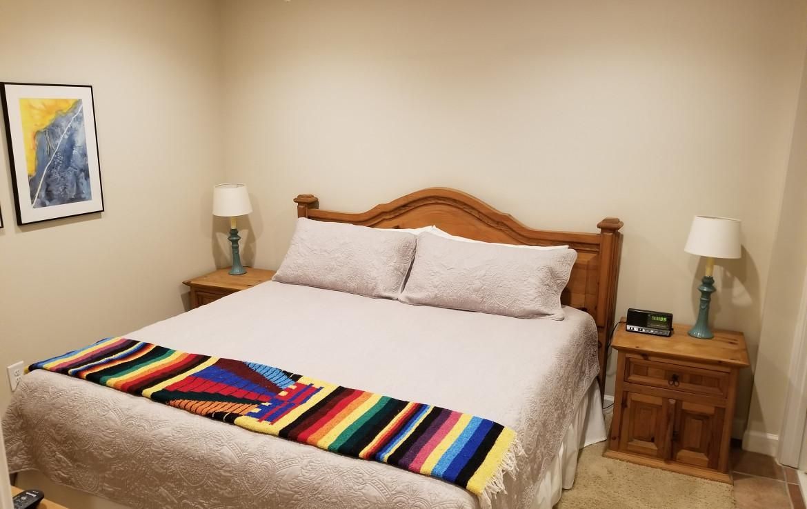 Bedroom with wooden bed, bedside tables, lamps, and colorful blanket on bed. Artwork on wall.