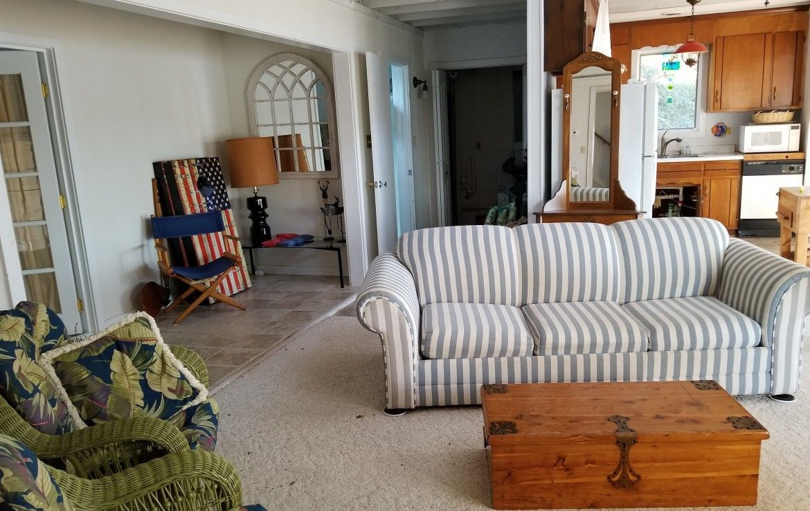 Living room with striped couch, wooden trunk, and access to kitchen.