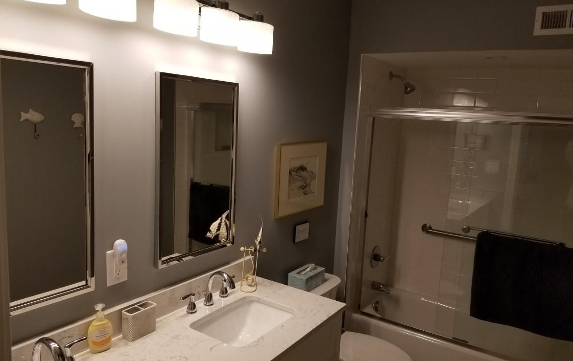 Bathroom with gray walls, white sink, and bathtub. Mirrors, light fixtures, and artwork are visible.
