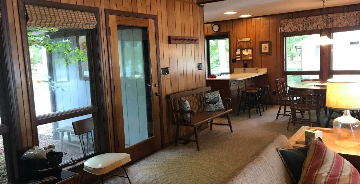 Wooden-paneled living room with glass doors and windows, a bench, and a dining area visible.