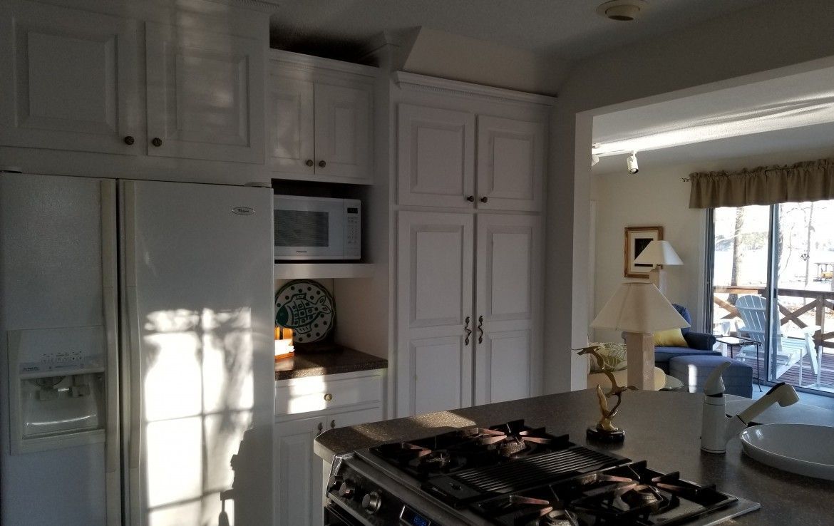 White kitchen cabinets, refrigerator, microwave, and range.  View of living area in the background through an archway.