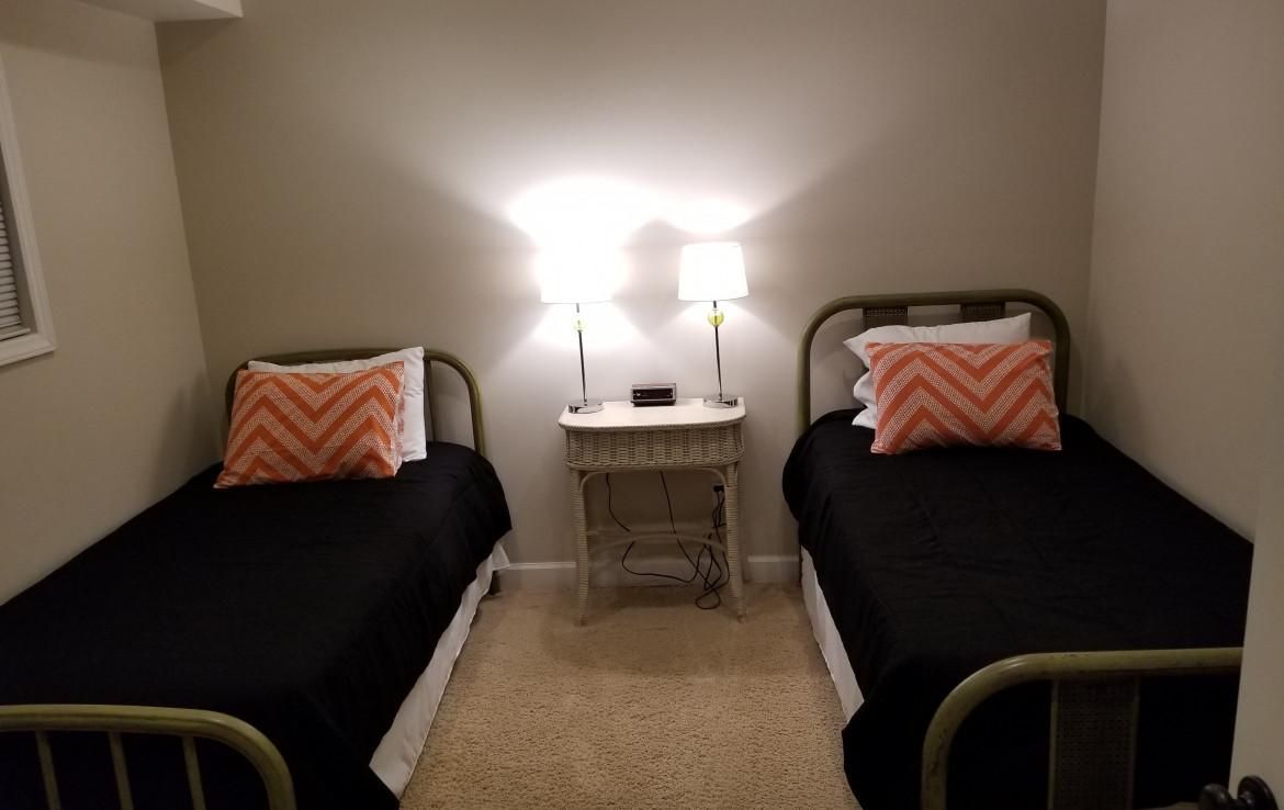 Two twin beds with black blankets, matching pillows, and a nightstand with lamps in a small room.
