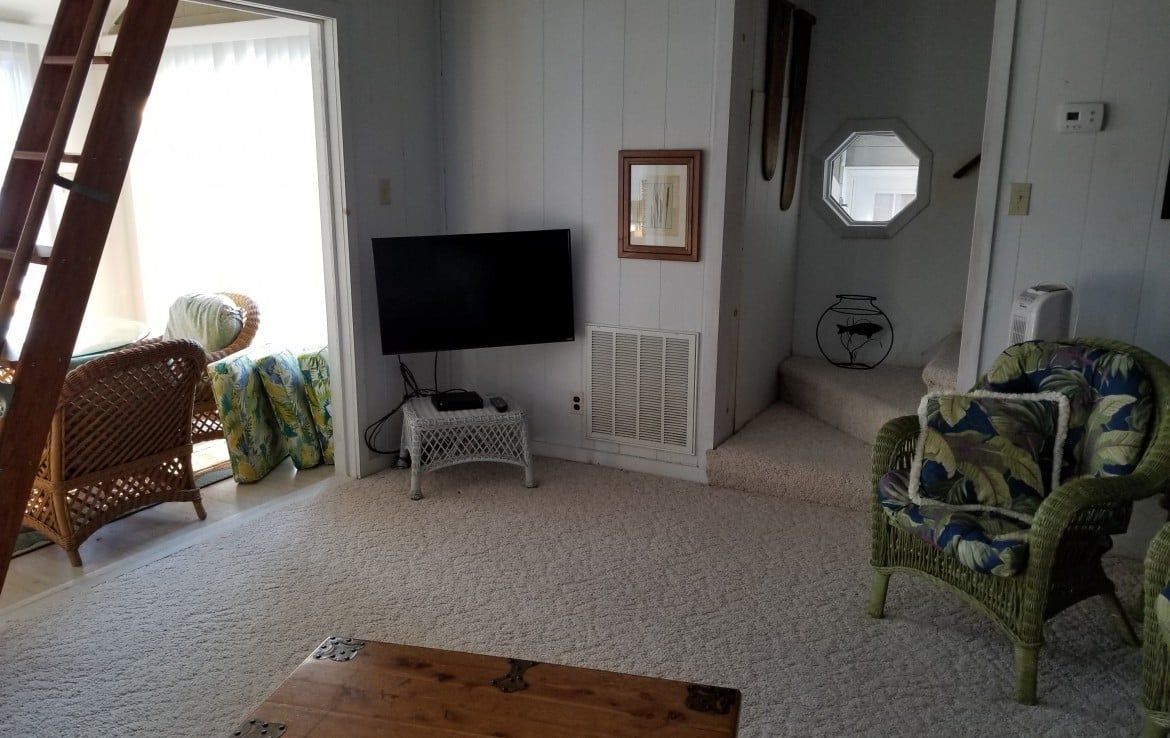 Living room with TV on wall, wicker furniture, and open doorway.