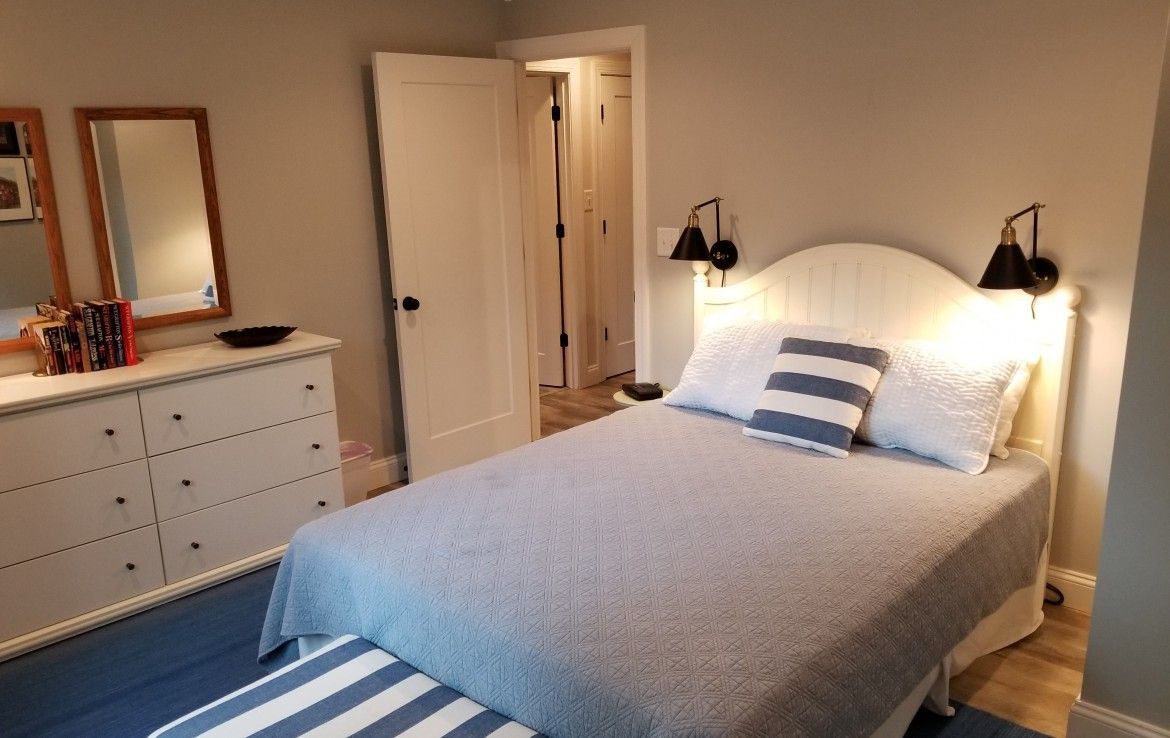 Bedroom with a white dresser, bed with a blue and white striped pillow, and sconce lighting.