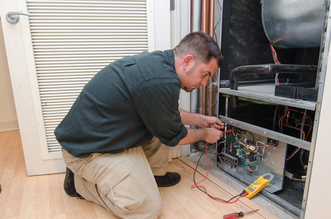 a man is kneeling on the floor working on an air conditioner furnace.