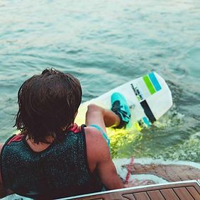 A man is sitting on a boat holding a wakeboard in the water.