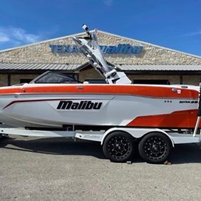 A red and white malibu boat is parked in front of a building.