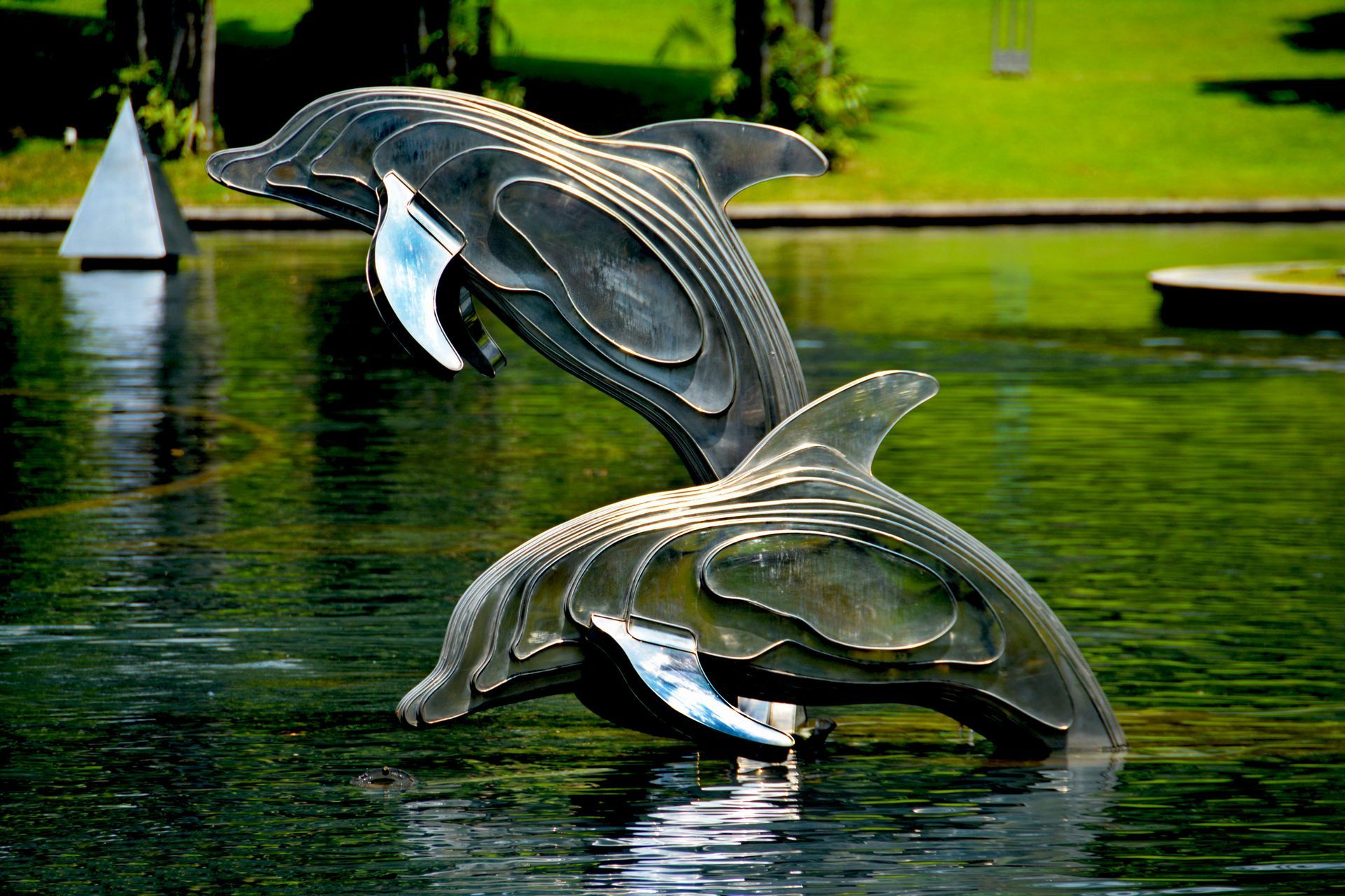 Two metal dolphin sculptures in a pond, one leaping, the other submerged; green water.