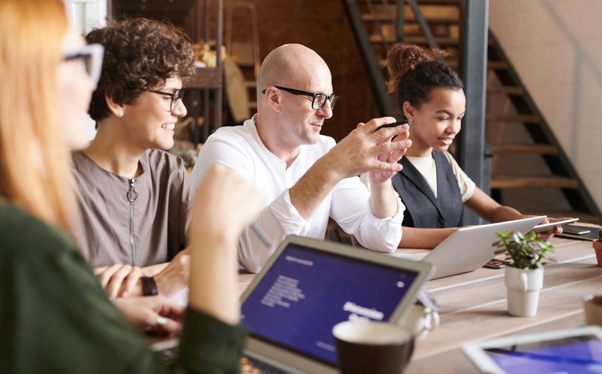 A group of people are sitting around a table with laptops.