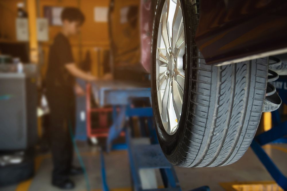 Car tire raised on a lift in a repair shop, mechanic in the background.