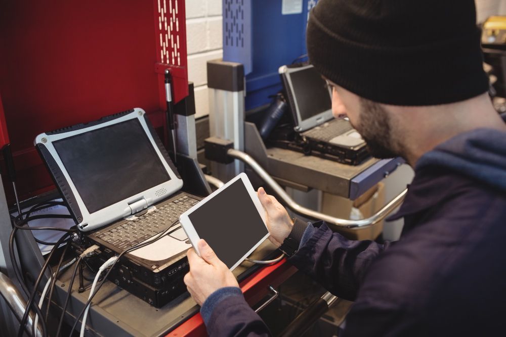 Mechanic using a tablet while working with diagnostic equipment in a repair shop.