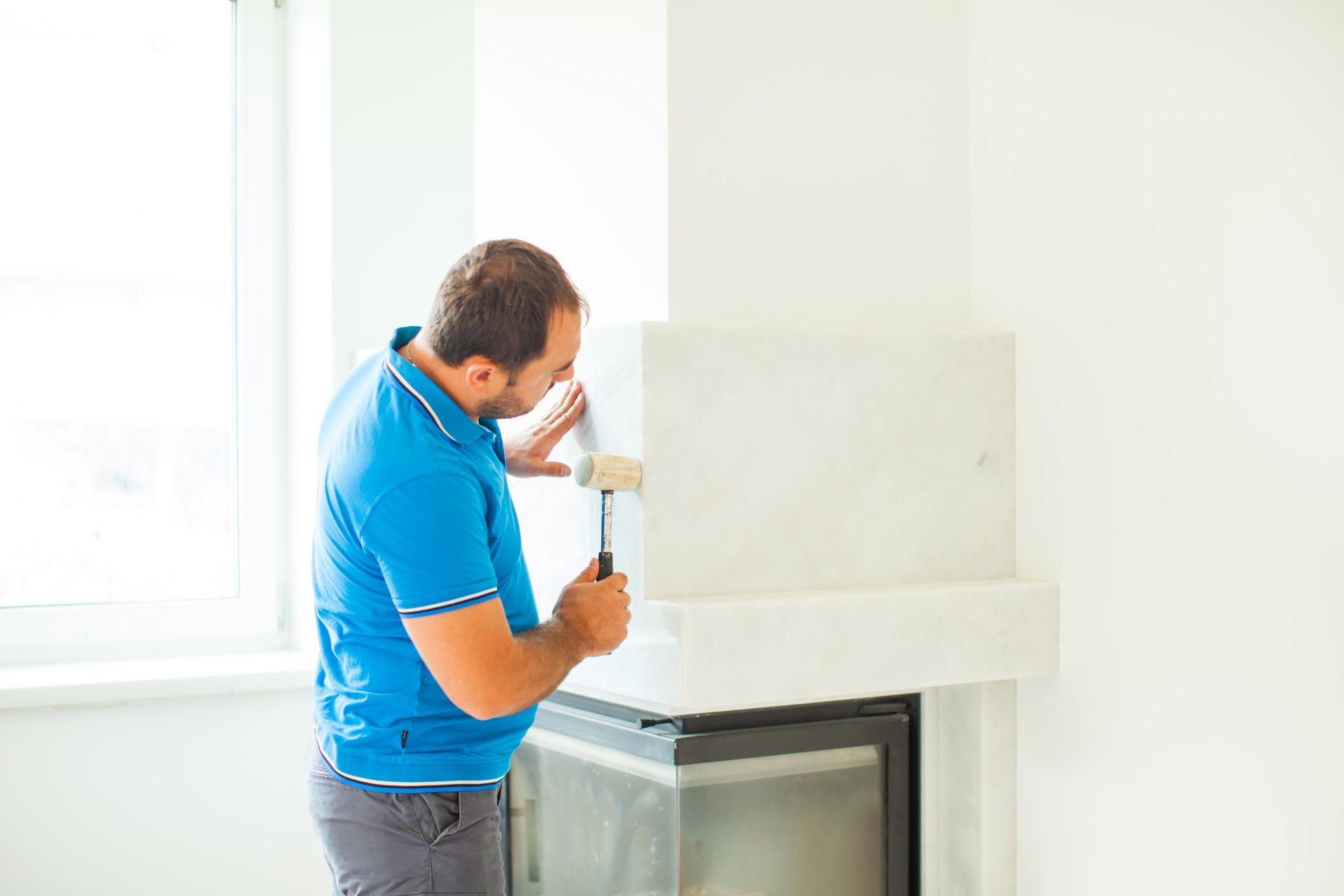 A man is fixing a fireplace with a hammer in a living room.