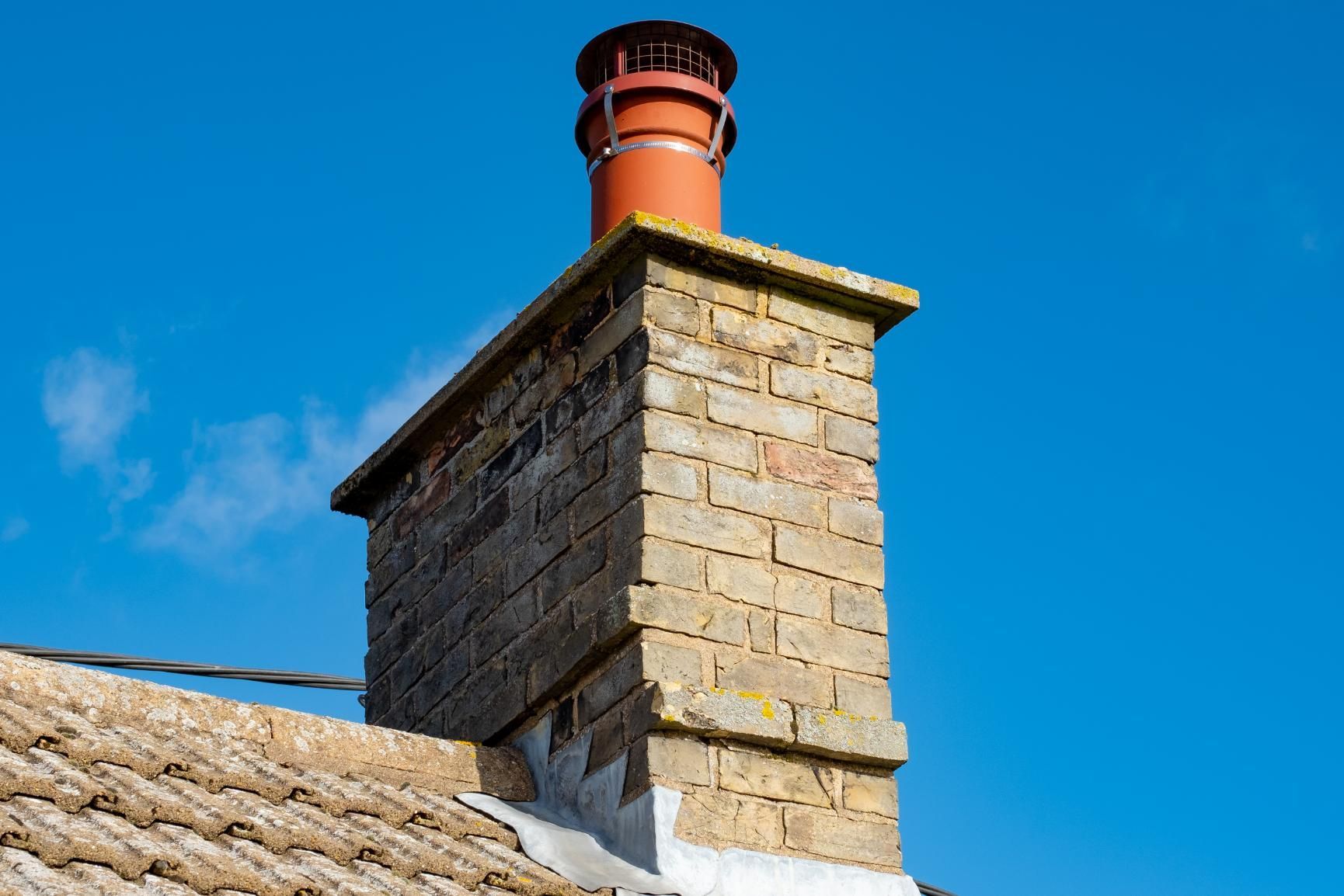 A brick chimney on top of a roof with a blue sky in the background.