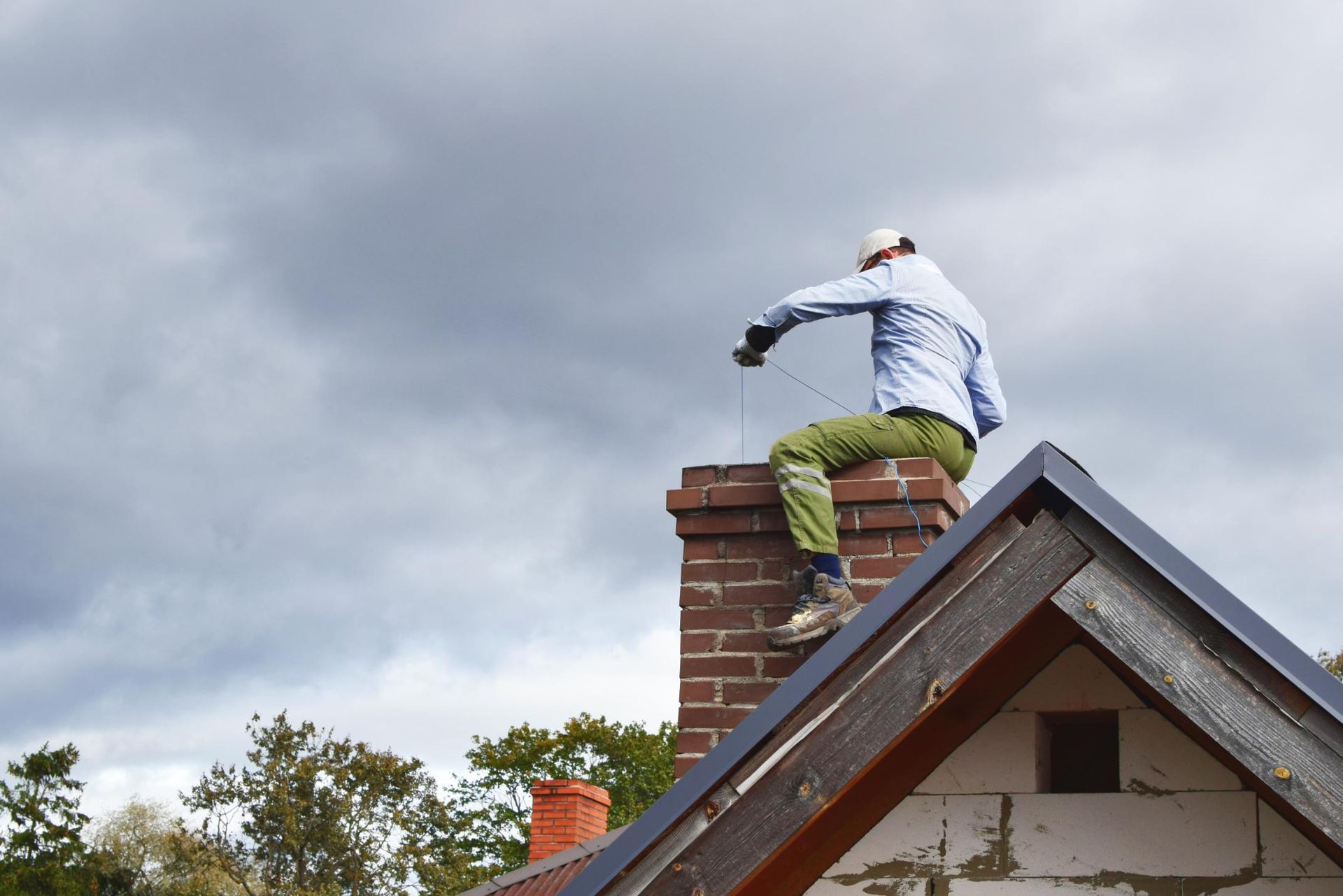 A man is sitting on top of a brick chimney on the roof of a house.