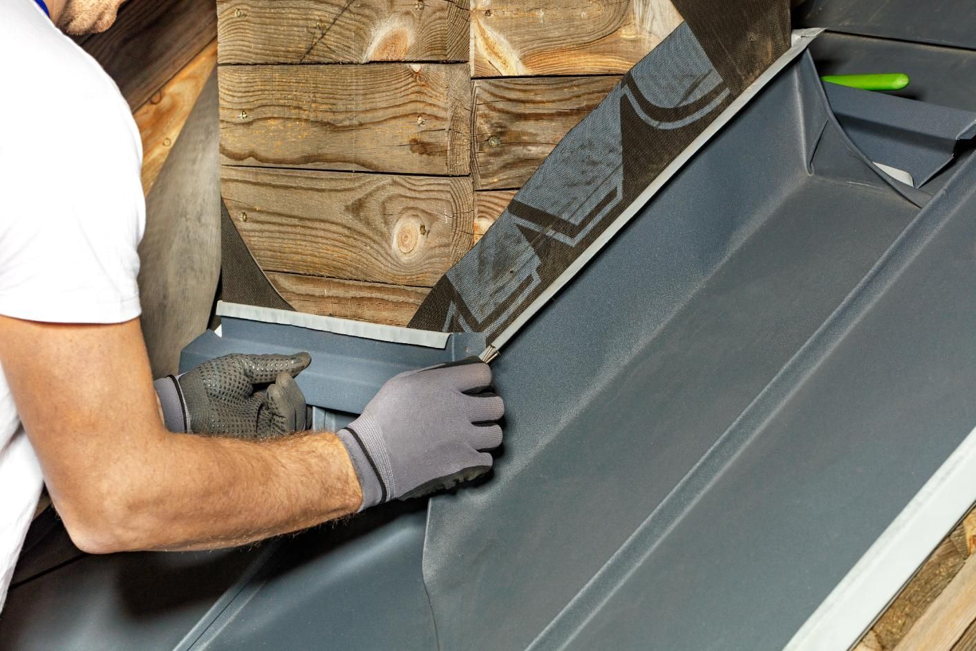 A man wearing gloves is working on a roof.