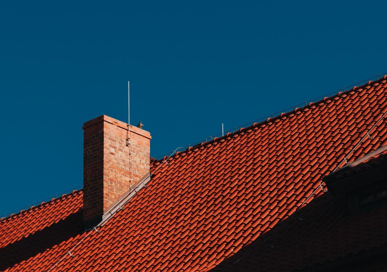 A red tiled roof with a chimney on top of it against a blue sky.