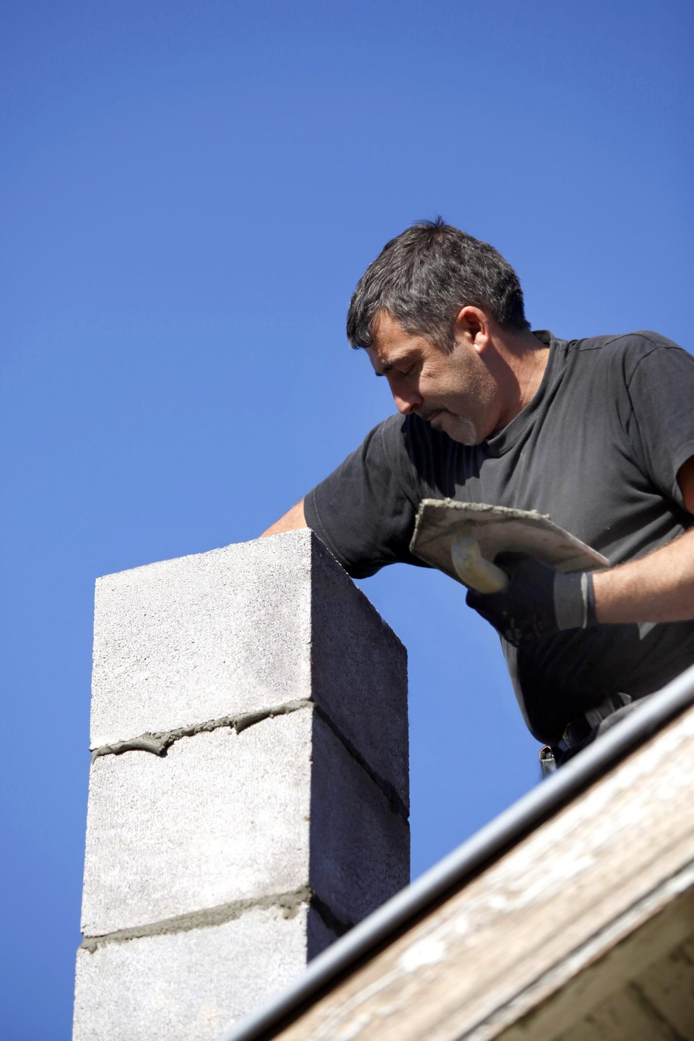 A man is working on a chimney on top of a building.