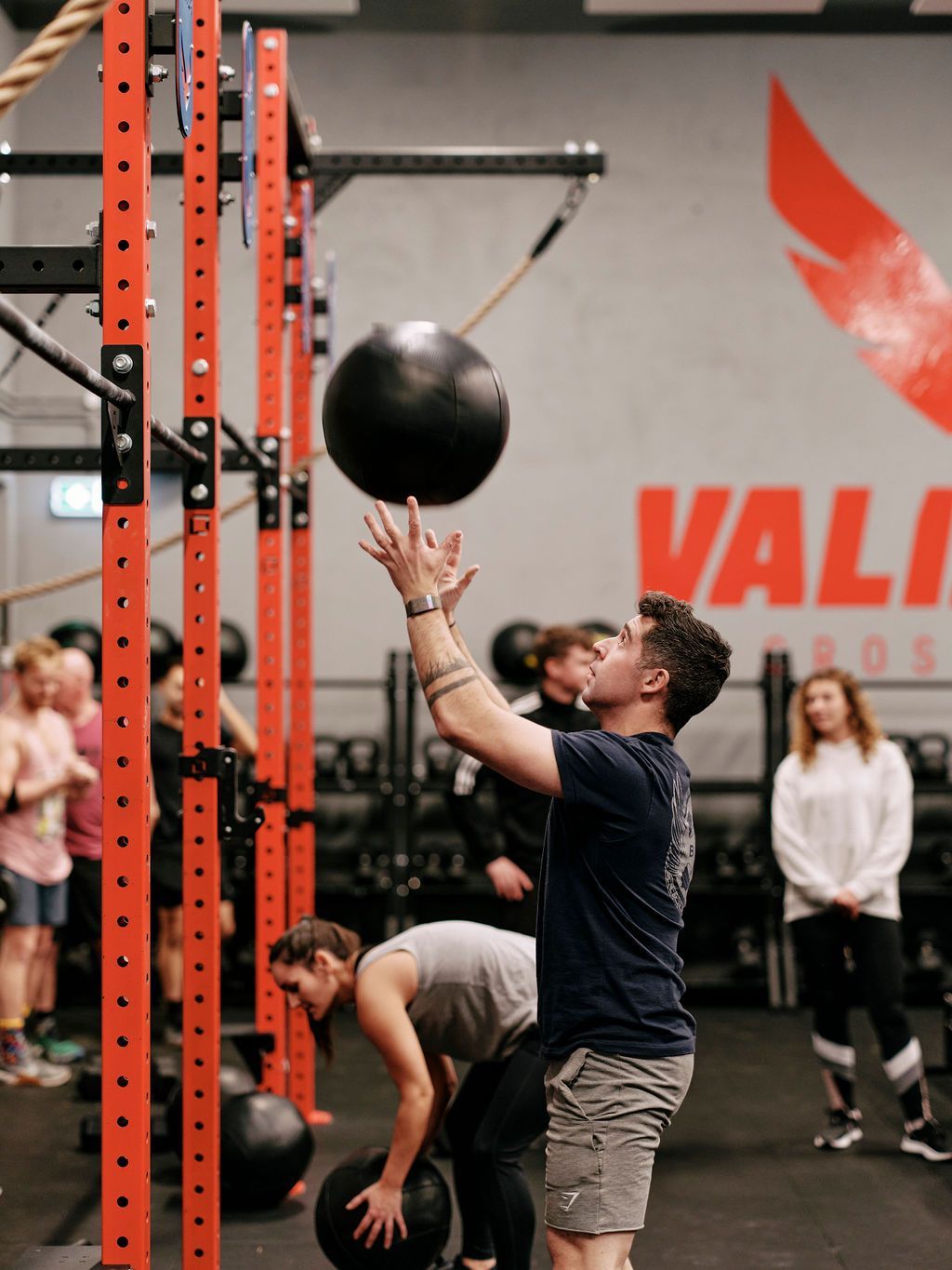 A man is throwing a medicine ball in a gym with the word vali on the wall