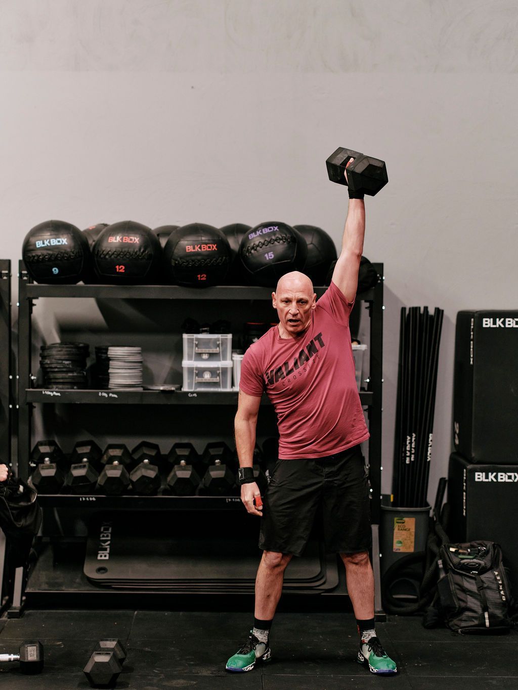 A man is lifting a dumbbell over his head in a gym.