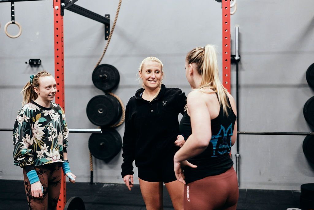 Three women are standing in a gym talking to each other.