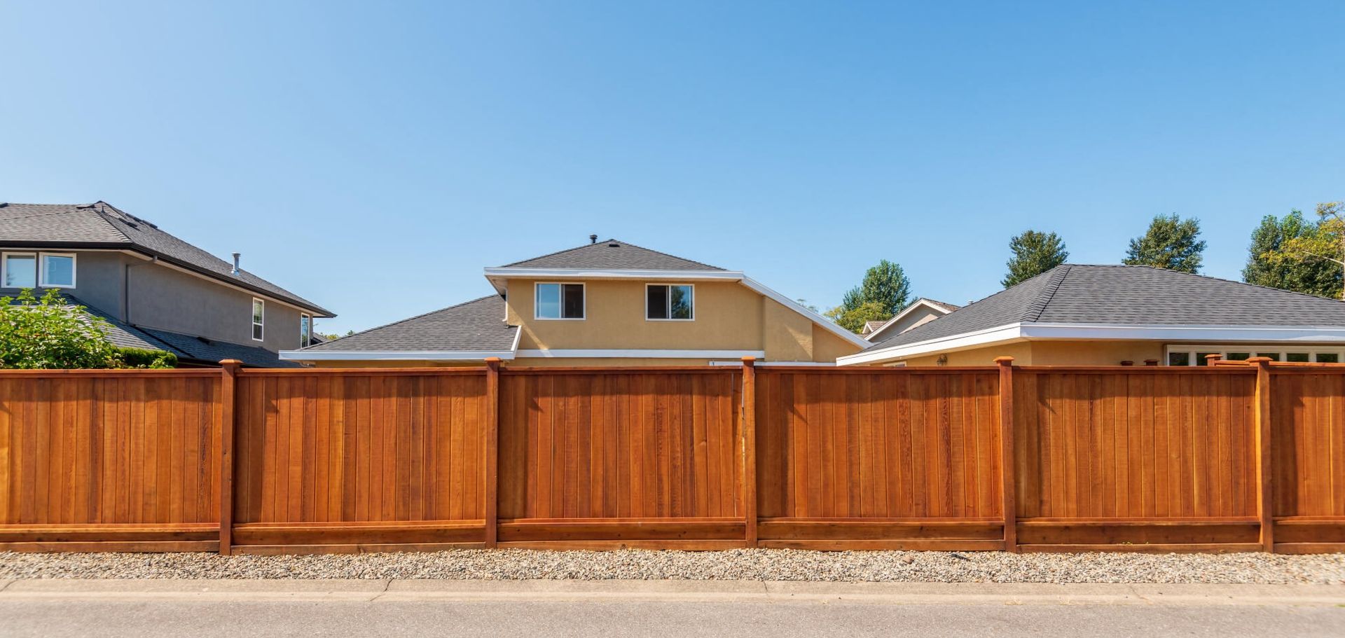 Redwood fencing surrounds a residential area with houses in the background.