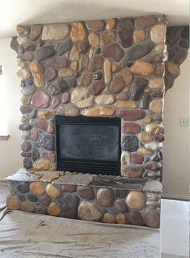 Fireplace with stone surround, a black metal firebox and glass doors. A painting hangs above.