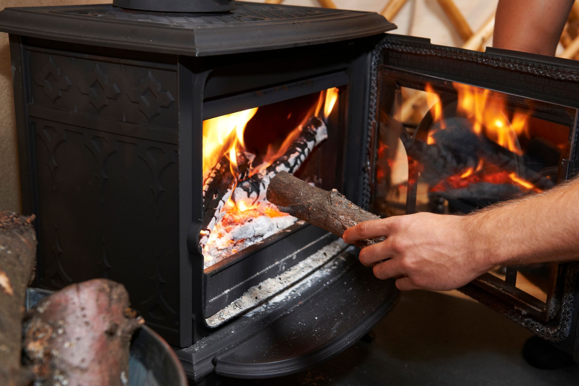 Person adding a log to a lit wood-burning stove with flames visible inside, indoor setting.