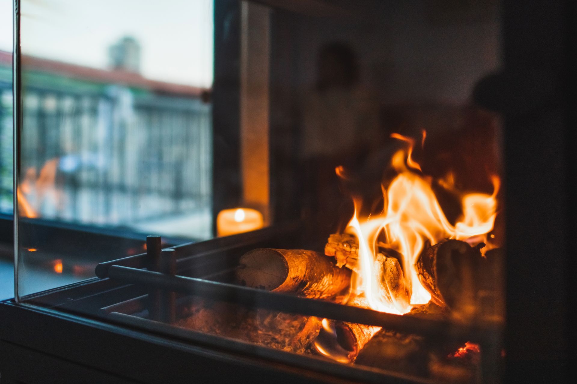 Fire burning in a fireplace with a blurred outdoor scene visible through glass.